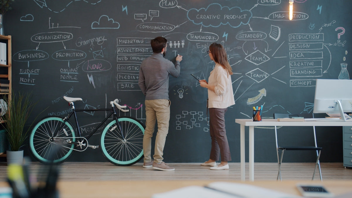 Two people drawing on a chalkboard wall.
