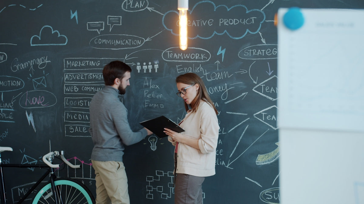 Two people discussing a business plan on chalkboard.