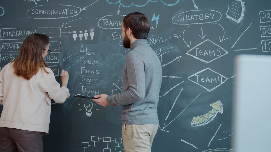 Two people planning on a chalkboard with diagrams.